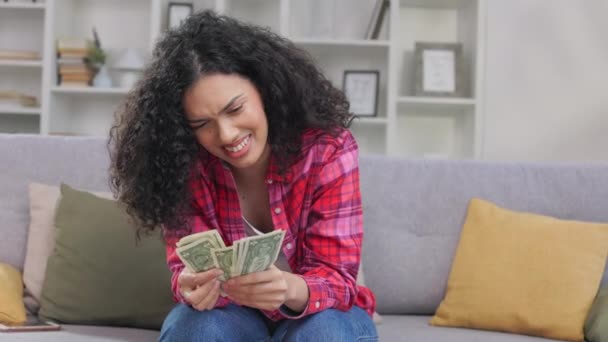 アフリカ系アメリカ人の成人女性は ジーンズとシャツを着てソファーに座り ドル紙幣を数える 絶望的な女性はお金の欠如を感じ 紙幣を揺さぶり 捨てる — ストック動画