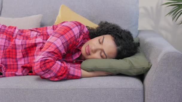 屋内での午後の時間帯に快適なソファーで寝ているカラフルなシャツの若い暗い髪の女性 アフリカ系アメリカ人女性 自宅での身体的および精神的な仕事の後に力を取り戻す — ストック動画