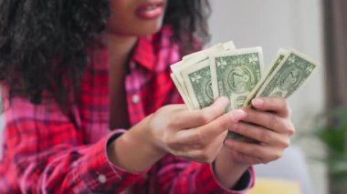 Parayla başı dertte olan bir kadına yakın çekim. Parlak kareli gömlek giyen Afro-Amerikan kadın dolar sayıyor ve hayal kırıklığı yaşıyor. Fon eksikliği kavramı.