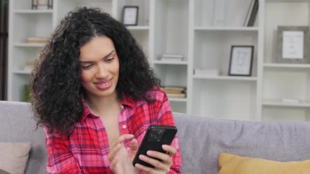 アフリカ系アメリカ人女性がボーイフレンドとオンラインメッセンジャーでチャットし デートの時間を手配します スマートフォンを握るカジュアルなウェアを着た笑顔の女性は 遠ざかって夢を見る — ストック動画