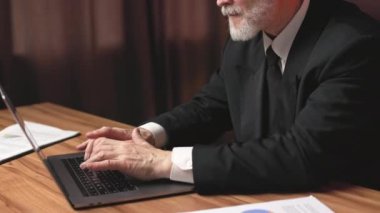 İş elbisesi giymiş üst düzey bir şahsın rahat iş yerinde dizüstü bilgisayardan kelimeleri arama motoruna girerken görüntüsü. İnternet tarayıcısı üzerinden bilgi arayan gözlüklü gri saçlı bir profesyonel..