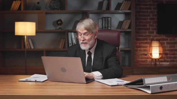 在写字台通过现代手提电脑回复电子邮件的一位戴眼镜的老年绅士的前照 利用工作中的数字技术管理个人效力的有经验的企业家 — 图库视频影像