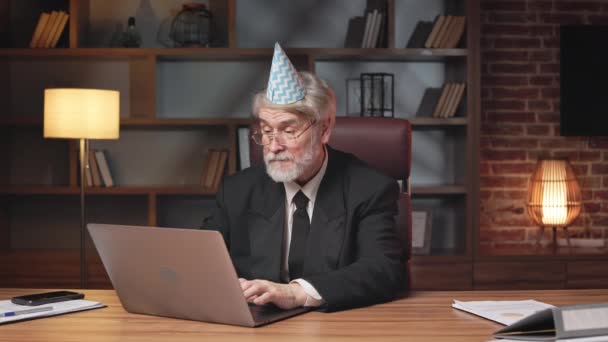 仲間の成功のお祝いを開始する前に オフィスのラップトップで働くパーティーコーン帽子の忙しい年上の男性 灰色の髪の起業家は緊急のタスクを終えた後休日の準備をする — ストック動画
