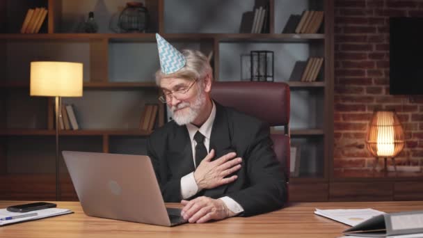 フォーマルウェアとパーティーコーンハットの高齢者は コンピュータ上のオンライン会議コールを介して暖かい願いを聞く グレイ髪のビジネスエグゼクティブ 会社記念日の議会に感謝 — ストック動画