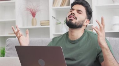 Sakallı serbest çalışan erkek bilgisayar ekranına bakarken şans diliyor. Hintli genç adam koltukta otururken modern bilgisayarı hayal kırıklığıyla kapatıyor..