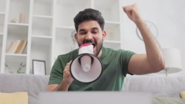 Kablosuz bilgisayarda video konferansı sırasında megafonla konuşan sakallı Hindistanlı adam. Erkek girişimci evde oturuyor ve yeni iş projesi için partnerlerini kışkırtıyor.
