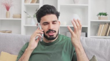 Gri koltukta oturan sakallı Hintli adamın portresi, aktif bir şekilde el kol hareketi yapıyor ve modern akıllı telefondaki canlı konuşmalar sırasında hayal kırıklığını dile getiriyor. İnsan kavramı, aletler ve zorluklar.