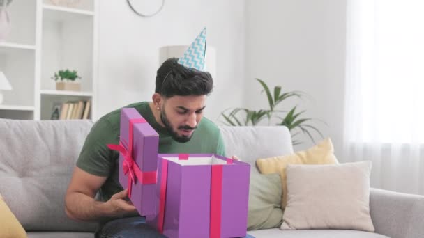 ピンクの箱の中を見つめ 嫌悪感で消えていくブルネット男 デザイナーのリビングルームで誕生日プレゼントで悲しみを感じるインド国籍の不満の男 — ストック動画