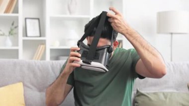 Hintli erkek, VR gözlük takıyor ve içeride 3D video izlemeye hazırlanıyor. Neşeli adam kişisel dairede rahat koltukta otururken sanal gerçeklik oyunları oynuyor..