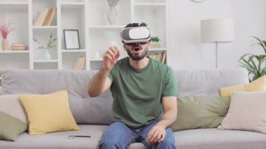 Sanal gerçeklik oyununun keyfini çıkarırken kişisel dairedeki kanepede oturan konsantre Hintli erkek VR gözlük takıyor. Kendine güveni olan, sıradan kıyafetler giymiş, elleri havada el kol gezen bir adam..