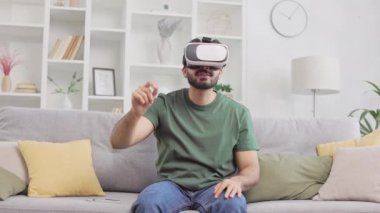 Genç sakallı serbest çalışan ve evde kanepede otururken VR gözlüğü kullanan biri. Bilgisayar programlarını kontrol eden ve sanal sayfaları çeviren pozitif Hintli adam.