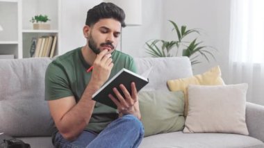 Düşüncelerini kendi gizli günlüğüne kaydeden düşünceli Hintli adam oturma odasında iç dekorasyonuyla dinleniyor. Sırıtan erkek, hayatı düşünüyor ve kapalı alanda kalemle notlar alıyor..