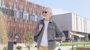 Çantalı ve e-scooter 'lı ilerici emekliler şehir merkezinde gezinirken faiziyle etrafa bakınıyorlar. Gri sakallı yakışıklı erkek modern binalara hayran..