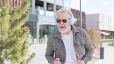 Şehir içinde yürürken kulaklıklı, şarkı söyleyen ve sokak dansı yapan mutlu yaşlı bir adam. Güneş gözlüklü olumlu büyükbaba dışarıda vakit geçiriyor ve boş zamanlarının tadını çıkarıyor..