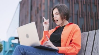 Düşünceli bir kadın çenesini eliyle tutuyor ve modern bina arka planında bilgisayar yazarken eureka hareketi yapıyor. Kurumsal sorunların çözümü için fikirler üreten başarılı bir uzaktan çalışan..