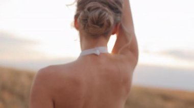 Çekici beyaz kadın kolları açık ve başı açık hareket ediyor ve tarımsal alanda geriye doğru eğiliyor. Açık havada şeffaf beyaz elbise giyen güzel bir kadın..