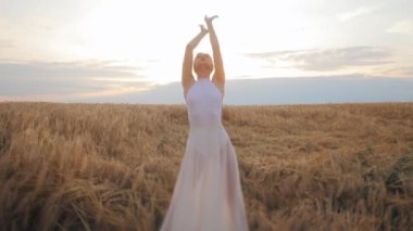 Beyaz bir kadının sahada dans edişini ya da zarifçe hareket edişini ön planda görmek. Beyaz elbiseli çekici bir kadın altın arka planda güzel bir tezat oluşturuyor. Gün batımı ve güzel hava.
