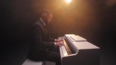 Konsantre olmuş adam klavyenin başında oturuyor ve parmaklarının hassas hareketiyle müzik yaratıyor. Beyaz piyanoda tekrarlama ve çalma sürecinde pratik yapan zarif erkek besteci.
