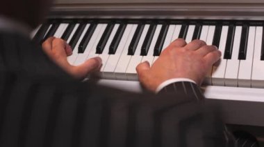 Yetenekli erkek avuçlarını siyah ve beyaz klavyelere dokundurarak müzik enstrümanında büyüleyici bir klasik melodi oluşturuyorlar. Ceketli yaratıcı adam piyano çalıyor ve en sevdiği hobiyi yapıyor..