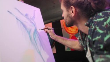 Mavi ve mor tonlarda tuval üzerinde resim yapma sürecinde olan yetenekli sanatçının yan görünüşü. Beyaz erkek, elinde boya fırçası tutarak sanat stüdyosunda şaheser yaratıyor..