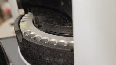 Eldiven giymiş laboratuvar çalışanı araştırma için test tüpleri yerleştiriyor. Bilimadamı, kimyasal bileşimi analiz etmek için özel bir cihazda malzeme içeren kapları düzenliyor..