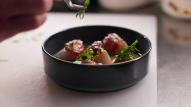 Şef 'in yeşil otlarla süslenmek için gurme yemeği ve cımbızı hazırlayışını yakından izleyin. Açık renkli tezgahta koyu yuvarlak kase. Restoran ve mutfak süreci kavramı.