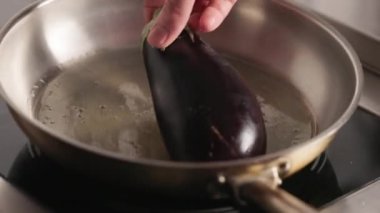 Çalışkan mutfak uzmanı taze mor patlıcan ve yeşil kapaklı patlıcan ısıtmalı metal tavayı yağ ile kaplıyor. Kızartma işlemi. Profesyonel yemek pişirmek için modern paslanmaz ekipman.