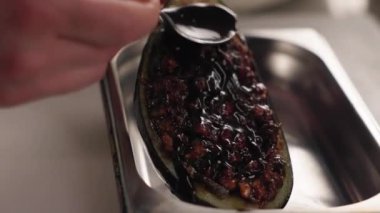 Izgara patlıcanın üzerine siyah sos döken kişiye yakın çekim. Mutfaktaki metal tepside iyi pişmiş sebze. Süsleme ve sunum kavramı.