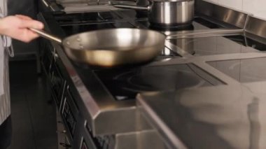 Modern mutfak ortamında fırını açarken kendine güveni tam bir yemek pişirme ve kızartma tavası kullanıyor. Çoklu yakıcı ve kontrol düğmeleri olan paslanmaz çelik yüzey.