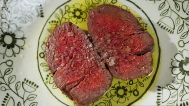 Yukarıdan, yağlı ve baharatlı seramik tabakta servis edilen orta pişmiş iki parça bifteğe bakın. Ortası kanlı sulu et yemeye hazır ve lüks restoranların ahşap masasında servis ediliyor..