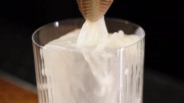 Bilinmeyen barmen, minyatür elek ve dolgu bardağıyla sıvı malzemelerin karışımını süzüyor. Şekil verilmiş buz küpü ferahlatıcı içecekle kaplanıyor ve soğuk içecek sıcaklığını koruyor..