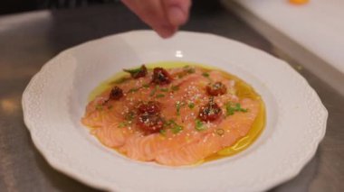 Şef somon carpaccio 'yu servis için hazırlıyor ve üstüne bir tutam parmesan peyniri ekliyor. Balık aperatifli yuvarlak beyaz tabak özel tat ve lezzet için ekstra katkı sağlıyor..