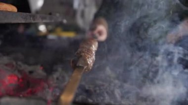 Izgaradan yükselen dumanla birlikte açık ateşte pişirilen şişlenmiş Lyulya kebabının yakın görüntüsü. Modern restoran mutfağında yemek pişirme eylemi.