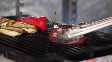 Barbeküde ızgara yapılan çeşitli yiyecekleri yakından izleyin. Patlıcan, kırmızı dolma biber ve biftek. Izgaradan duman yükseliyor ve şu anda yemek pişirildiğini gösteriyor..