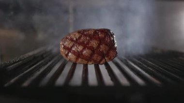 Bir parça taze biftek ve belirgin ızgara izleri. Dumanla bulanık bir arkaplan. Hazırlama işlemi devam ediyor. Barbekü ya da ev yemeği..