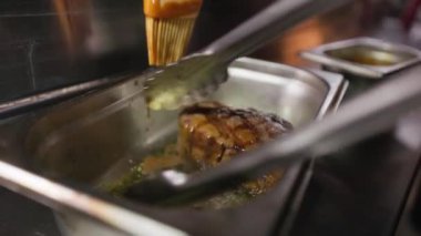 Bir parça sulu ızgara et metal tepside fırça kullanılarak koyu kahverengi sosla kaplanıyor. Mutfak malzemesi ve sunumundan dolayı profesyonel mutfak ayarları.