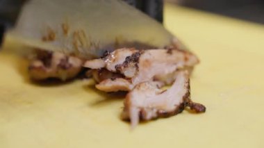 Dilimlenmiş et, sarı kesme tahtasındaki bıçakla kesiliyor. Hassasiyet ve dilimleme sürecinin içeriğine ve dokusuna odaklanmış. Yemek pişirme ve sunum kavramı.