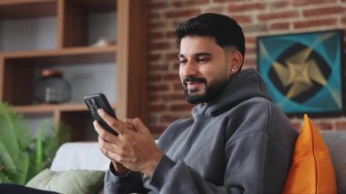 Hayalperest İspanyol adam cep telefonunu elinde tutuyor ve uzaktan konuşurken heyecanlı bir ifadeyle yan yana bakıyor. Genç gadget kullanıcısı evde takılırken çevrimiçi grup sohbetinde mesaj yazıyor.