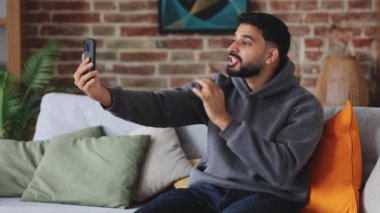 Dikkatsiz Hintli blogcu sosyal medya için kısa videolar kaydediyor ve yastıklı koltukta otururken parmaklarına güveniyor. Gülümseyen adam, başarı ve popülerlik kazanma adımlarını ve kuralları anlatıyor.