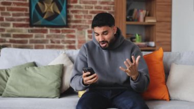 Kapüşonlu ve kot pantolonlu umut dolu erkek oturma odasında telefonla oynarken online kumarhanede zafer için dua ediyor. Çekici bir adam bahsin sonucunu beklerken umutsuzluğa kapılıp geri dönüyor..