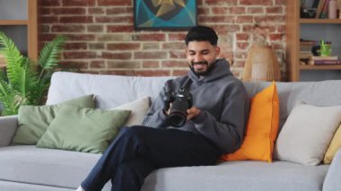 Mutlu Hintli fotoğrafçı objektifle profesyonel fotoğraf makinesi tutuyor ve daha önce çekilmiş fotoğraflara bakarken gülümsüyor. Yetenekli yaratıcı, müşteriye göndermeden önce işin sonucunu kontrol eder.