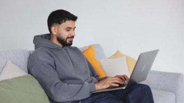 Koltuğunda oturan ve bilgisayarın klavyesinde el hareketleriyle yazı yazan Arap bir erkeğin yan görüntüsü. Kariyer için kişisel başvuru gönderen ve olumlu cevap alan neşeli adam..
