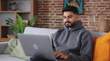 Dikkatsiz Hintli erkek, modern dizüstü bilgisayarını ayakta tutuyor ve dişlek bir gülümsemeyle ekrana bakarken daktilo çekiyor. Kulak delici sakallı adam yeni bilgisayarı test ediyor ve kullanılabilir fonksiyonları kontrol ediyor.