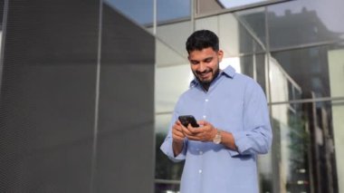 Şehirdeki iş yerinin önünde cep telefonu kullanan genç bir iş adamı. Gülümseyen, sakallı bir adamın şehirde dolanıp telefonda konuşması. İş kavramı, günlük