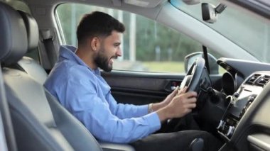 Mutlu yakışıklı adam içeride otururken yeni araba almaktan zevk alıyor. Koyu saçlı, neşeli bir adamın direksiyon simidini öpmesi, neşeli modern bir araç. Duygular kavramı, araba satın alma..