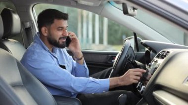 Resmi giyinmiş, cep telefonuyla konuşan ve arabada gülen yakışıklı sakallı adam. Şehirdeki araçtan arama yapmak için akıllı telefon kullanan gülümseyen genç bir adamın yan görüntüsü. Teknoloji, bağlantı kavramı.