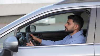 Ciddi sakallı bir adam cadde boyunca araba sürüyor, açık pencereden bakıyor. Mavi tişörtlü yakışıklı esmer erkek sürücü araç kullanırken kameraya bakıyor. Sürüş, yaşam tarzı konsepti