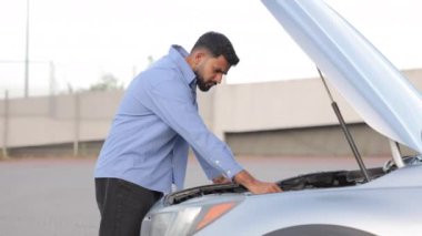Orta yaşlı şaşkın bir adam sokakta bozuk bir arabanın kaputuna bakıyor. Endişeli erkek sürücünün arabanın motorunu incelemesi, radyatörü tamir etmeye çalışması. Araba servisi kavramı.
