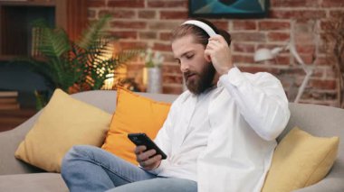 Uzun saçlı, beyaz kulaklık takan, rahat bir odada oturan ilham verici bir adam. Kafkasyalı bir adamın eğlendiği ön manzara, ses ritmiyle birlikte şarkı söylemesi, kulaklıkları ayarlaması. Müzik, ses konsepti.