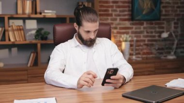 Sıradan beyaz gömlekli sakallı beyaz bir adam akıllı telefona bakarken masa başında oturmuş parmağını kaldırıyor. İnternetteki videodan sonra onaylayıcı yüz ifadesi takınıyor. Rahat ofis ortamında dinlenmek.